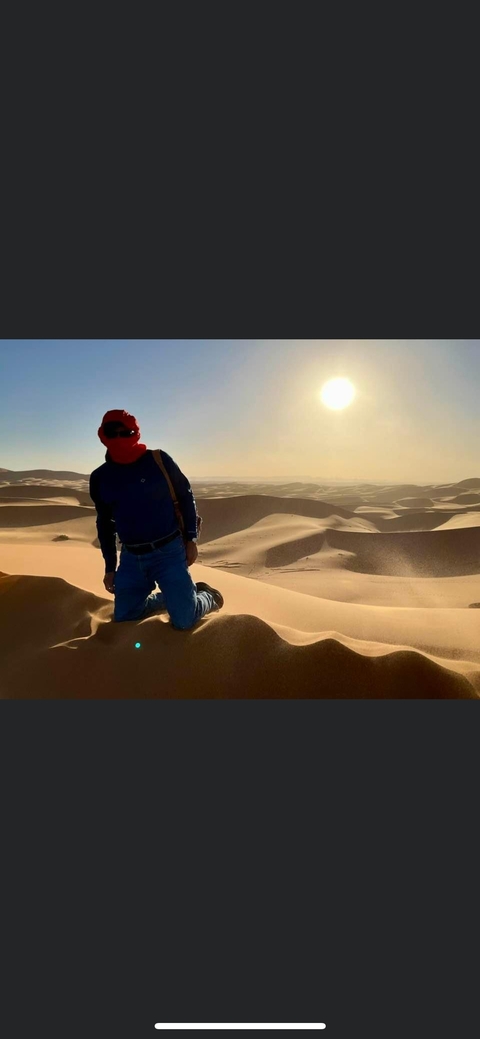Person kneeling in desert with sun setting in the background.