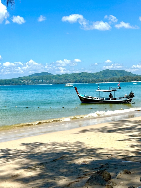 Longtail boat moored on a sunny beach with distant hills.