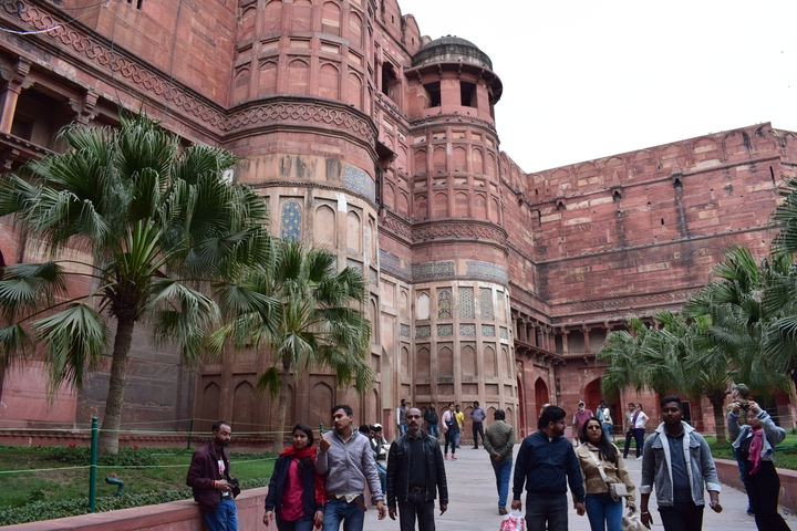 People walking in front of Agra Fort's red sandstone walls.