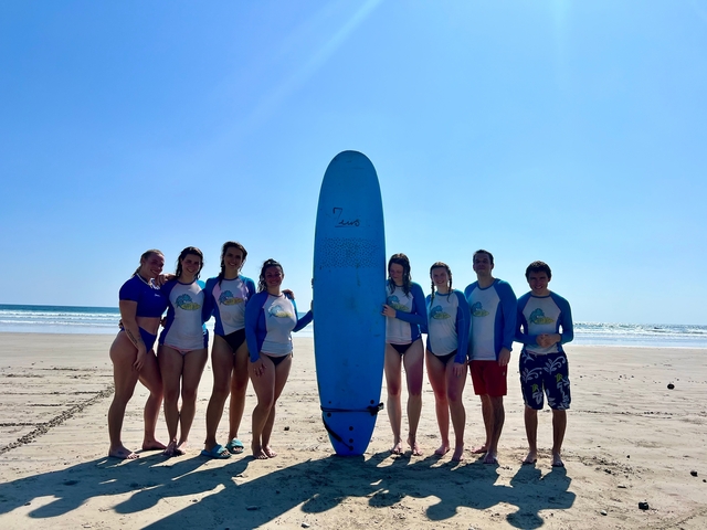 A group of people on a beach with a surfboard, wearing matching shirts.