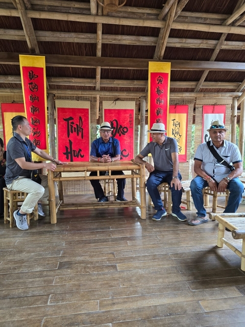 Men sitting at a wooden table with bright banners in the background.