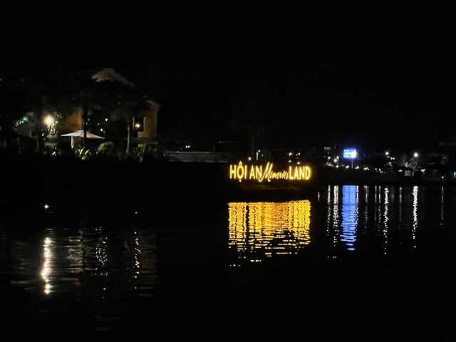 Illuminated sign 'Hoi An Memories Land' reflecting on water at night.