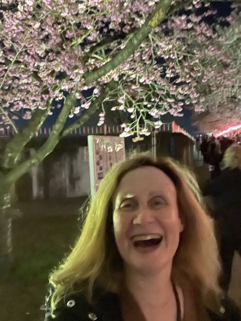 Person smiling in front of blooming cherry blossoms at night.