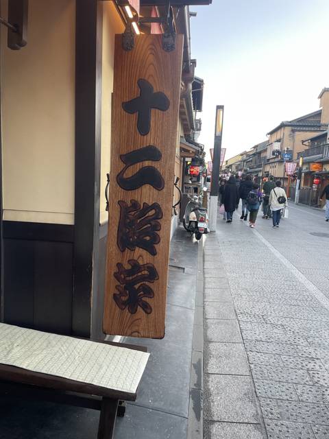 Japanese sign on a street with people and vehicles.