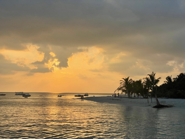 Beautiful sunset over a beach with silhouettes of people and boats.