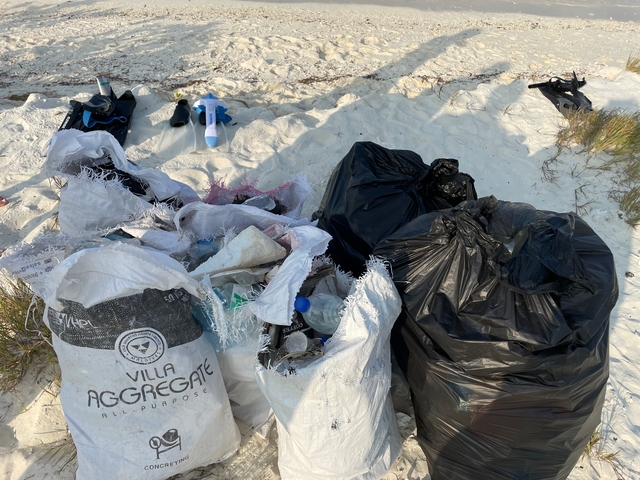 Bags of trash and diving equipment on a beach.