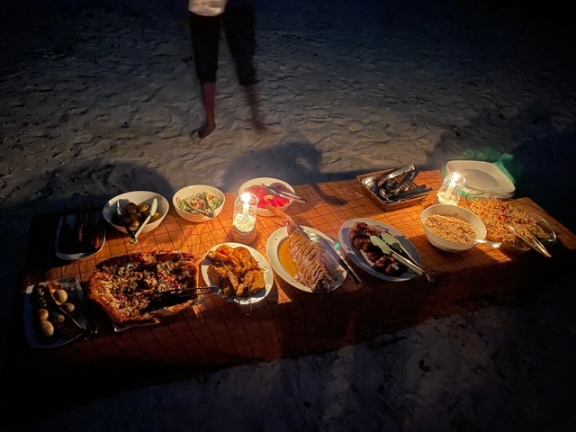 Table with a variety of dishes, including seafood, on a beach at night.