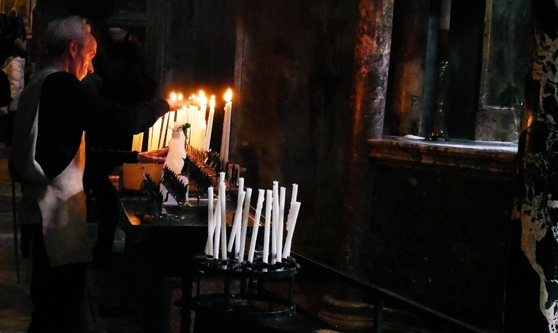 Person lighting candles in a dimly lit interior.