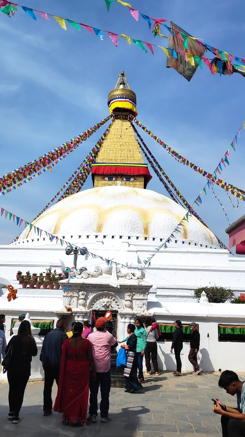 Large white stupa with prayer flags and eyes painted on it.