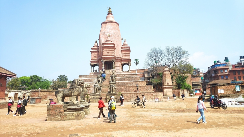People visiting a large brick temple with stone statues.