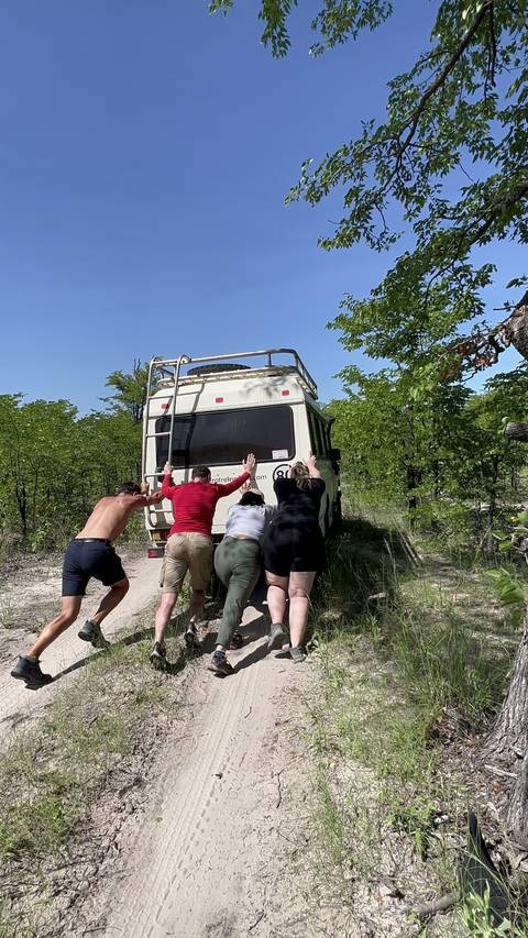 People pushing a stuck vehicle on a dirt road.