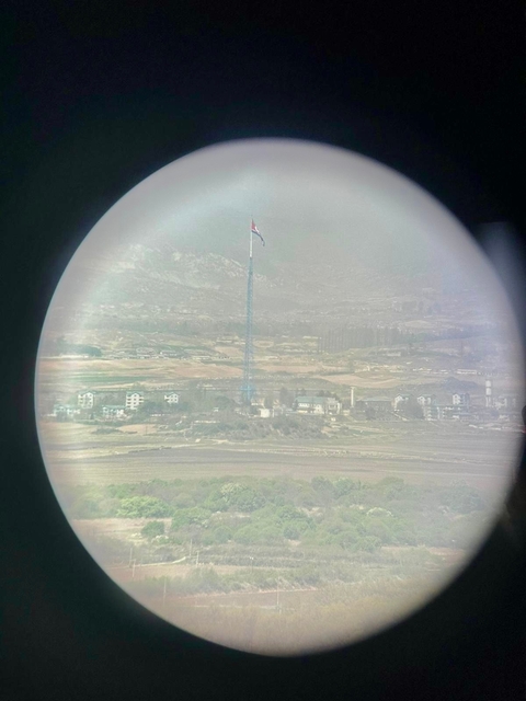 View through binoculars of a landscape with a tall tower and flag.