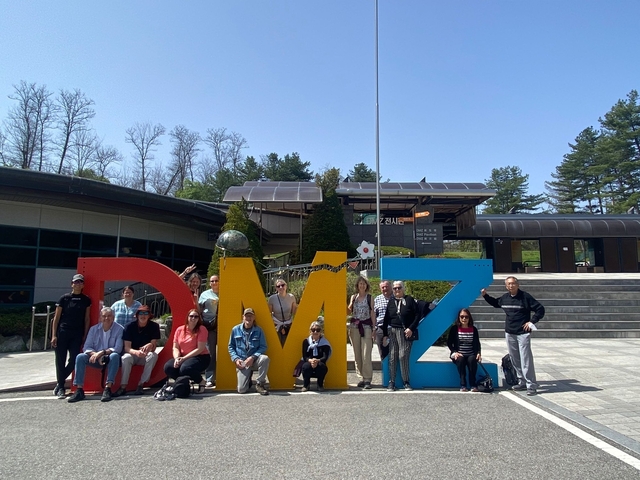 Tour group posing with large colorful letters spelling 'DMZ'.