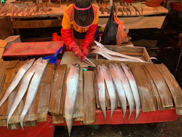 Market vendor preparing fish on a display table.