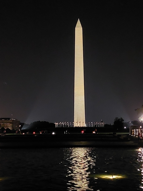 Washington Monument lit up at night with flags around.