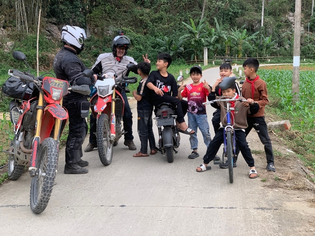 Two motorcyclists and local children on a rural road.