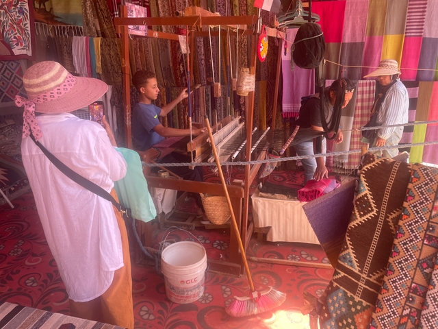 People working at a traditional weaving loom with textiles.