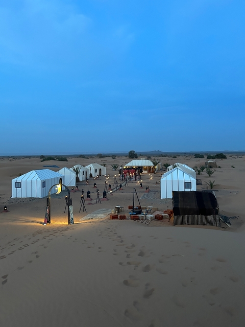 Desert camp setup with tents and lanterns at dusk.
