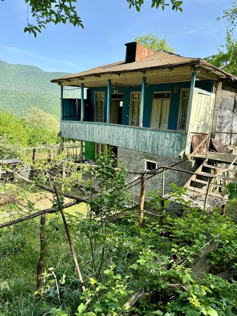 Old building with overgrown garden and stone structure.