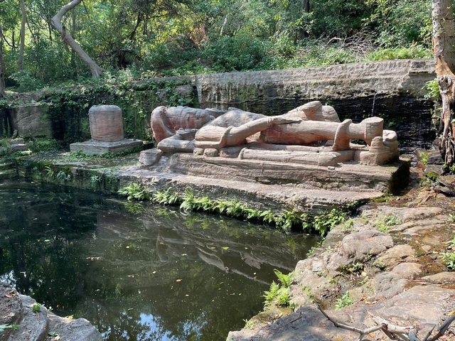 Stone sculpture by a water feature surrounded by greenery.