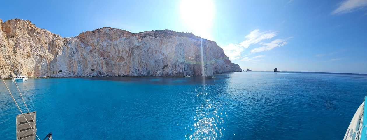 Rocky coastal cliffs with bright sunlight reflecting on the water.