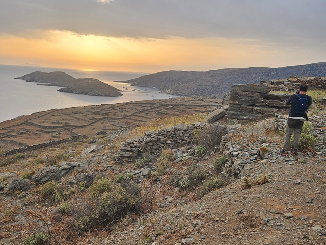 A person standing on a hill overlooking a scenic sunset over islands.