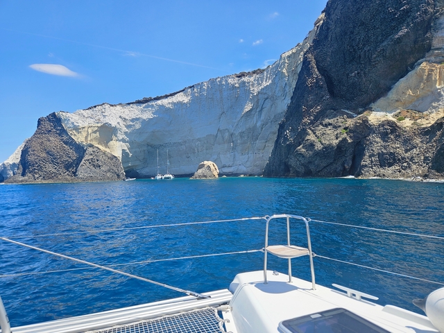 A boat on clear blue water with a backdrop of rocky cliffs.