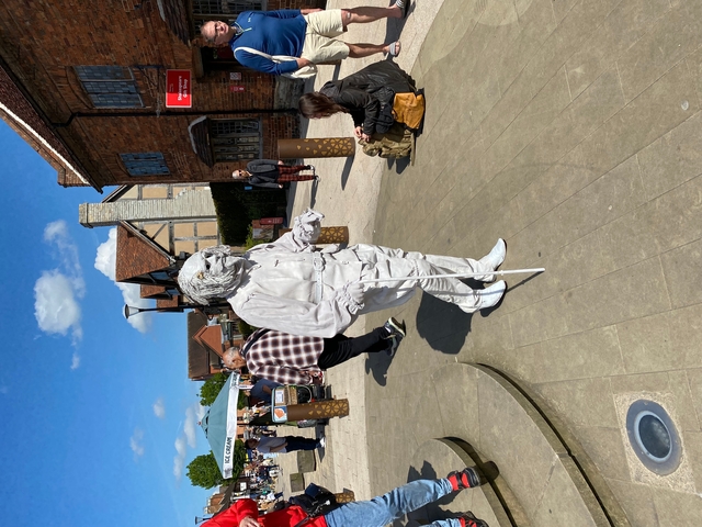 Street performer painted white standing in a busy square