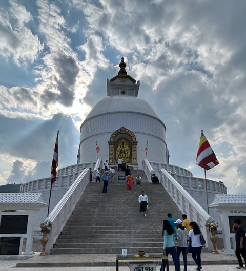 Large white stupa with people ascending the stairs.