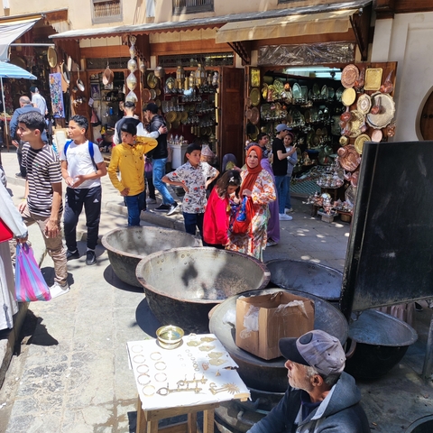 People shopping in a market with large copper pots.