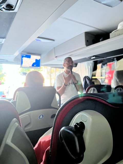 Tour guide speaking on a bus with a map screen.