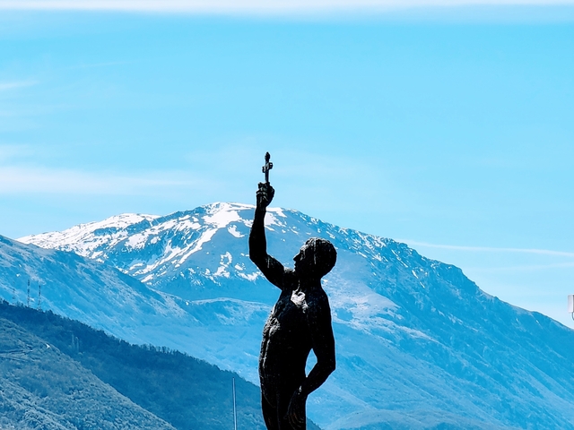 Statue holding an object with mountainous backdrop.