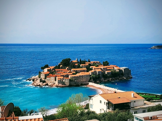 Island with red-roofed buildings surrounded by blue sea.
