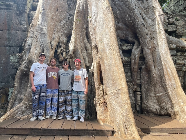 Four people standing in front of a massive tree with old ruins.