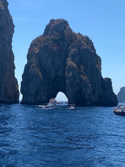Boats near the Faraglioni rock formations in a blue sea.