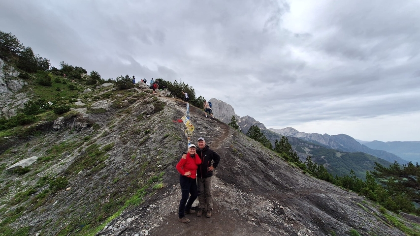 Two hikers standing on a mountain ridge with views of the surrounding peaks.