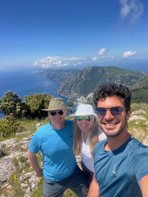 Three people taking a selfie with a mountainous coastal landscape.