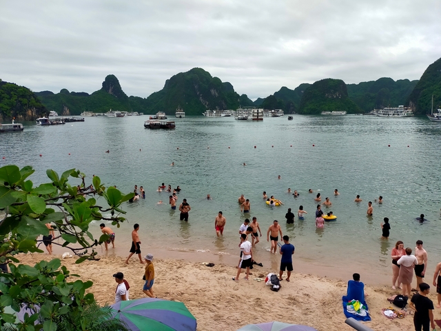 Beach scene with people swimming and boats in a bay.