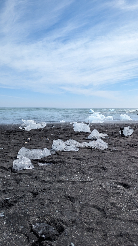 Pieces of ice scattered on a black sand beach by the ocean.