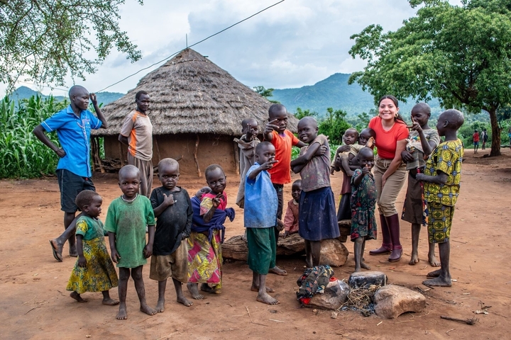 Group of children and a woman in front of a traditional hut.