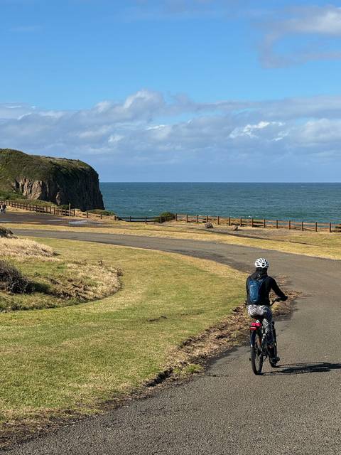 Cyclist on a path by the sea with cliffs.