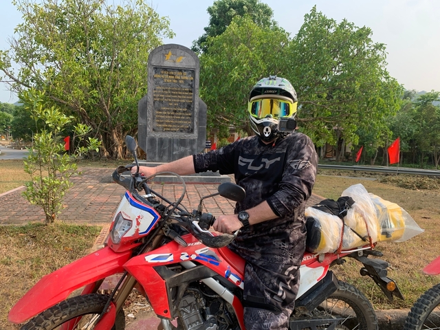 Motorcyclist posing in front of a monument with trees in the background.