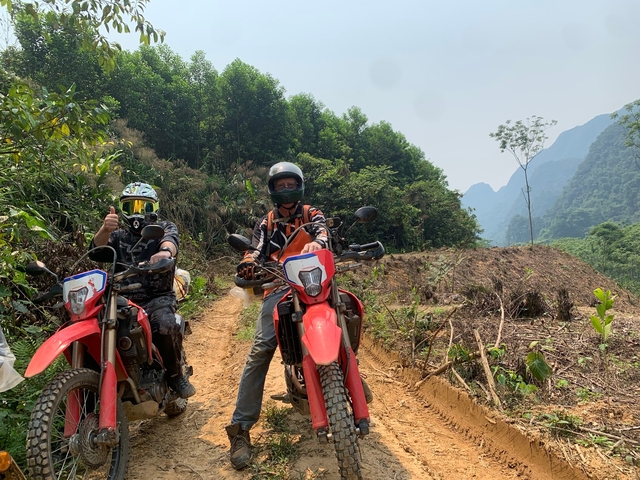 Motorcyclists on a dirt path with lush greenery.