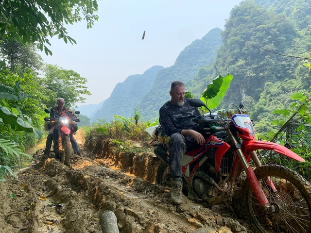 Motorcyclists resting on a rugged trail with scenic mountains.