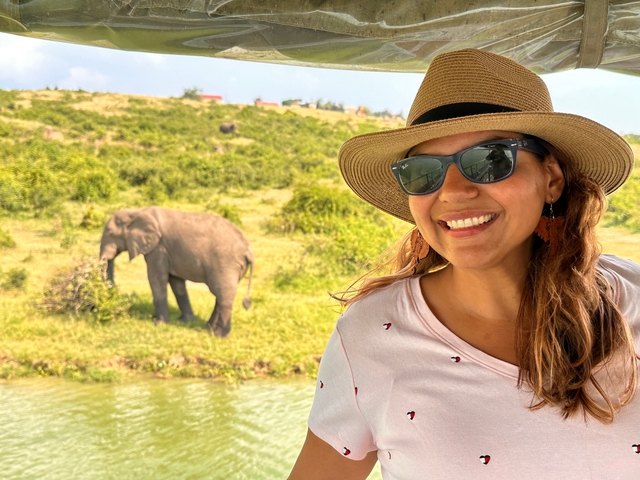 Person smiling with an elephant in the background near a riverbank.