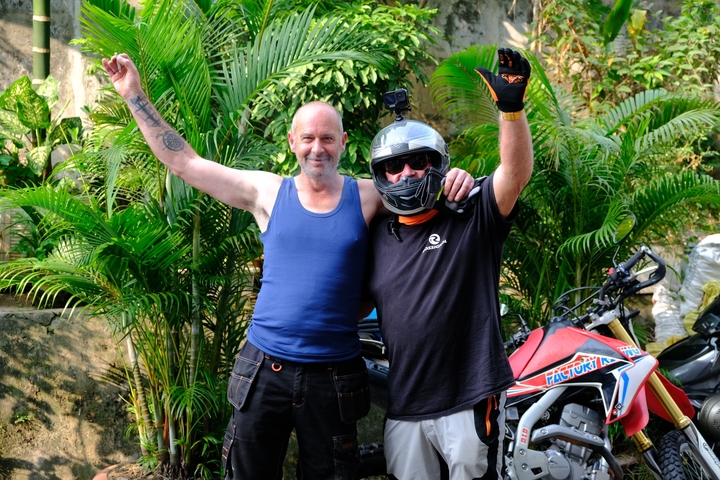 Two men posing with motorbikes, one wearing a helmet.