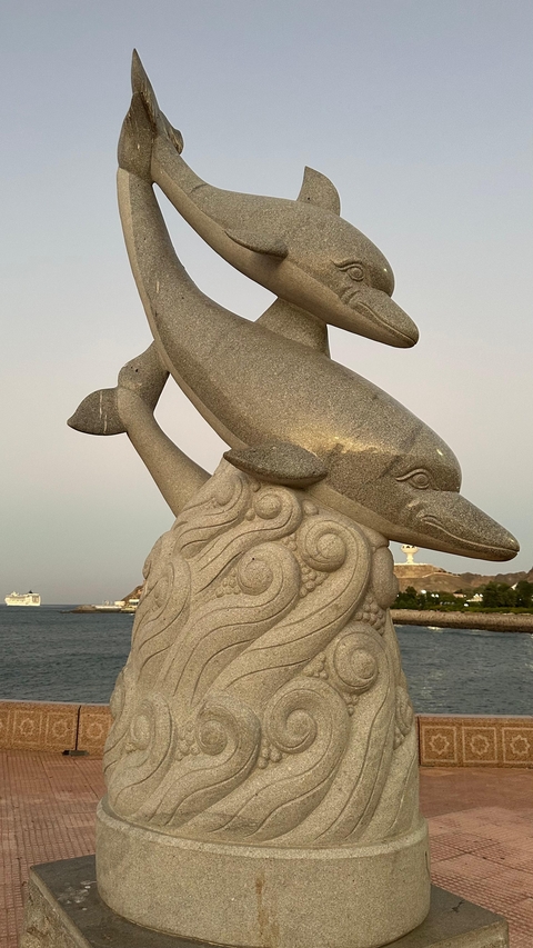 Stone sculpture of dolphins with a waterfront view.