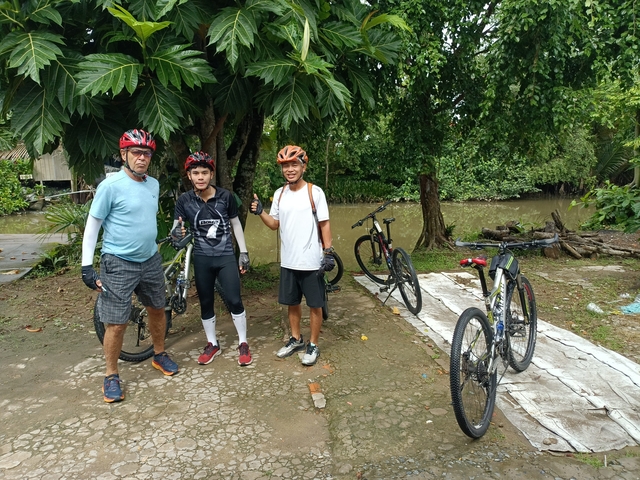 Group of cyclists posing with their bikes near water.