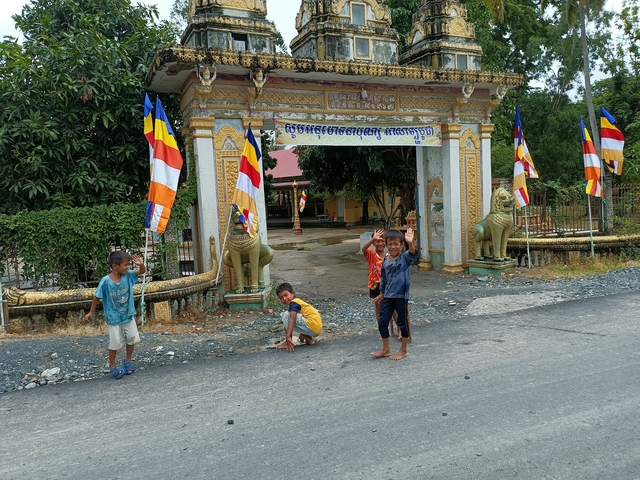 Children waving near a decorated entrance in Cambodia.