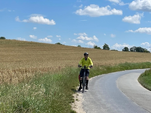 A cyclist on a rural road with fields on either side.